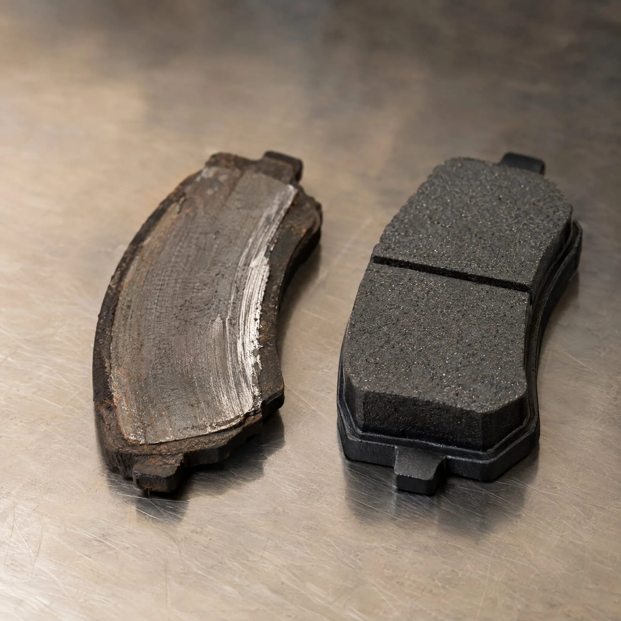 Worn brake pad next to a new brake pad on a workbench