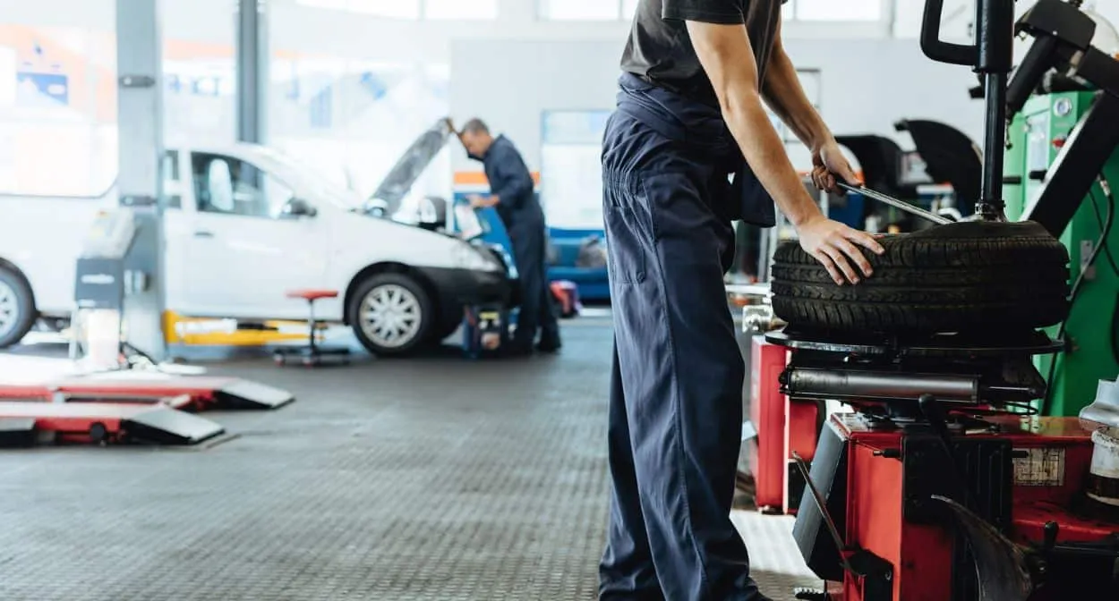 Technician mounting a tire on a tire changer in a busy repair shop