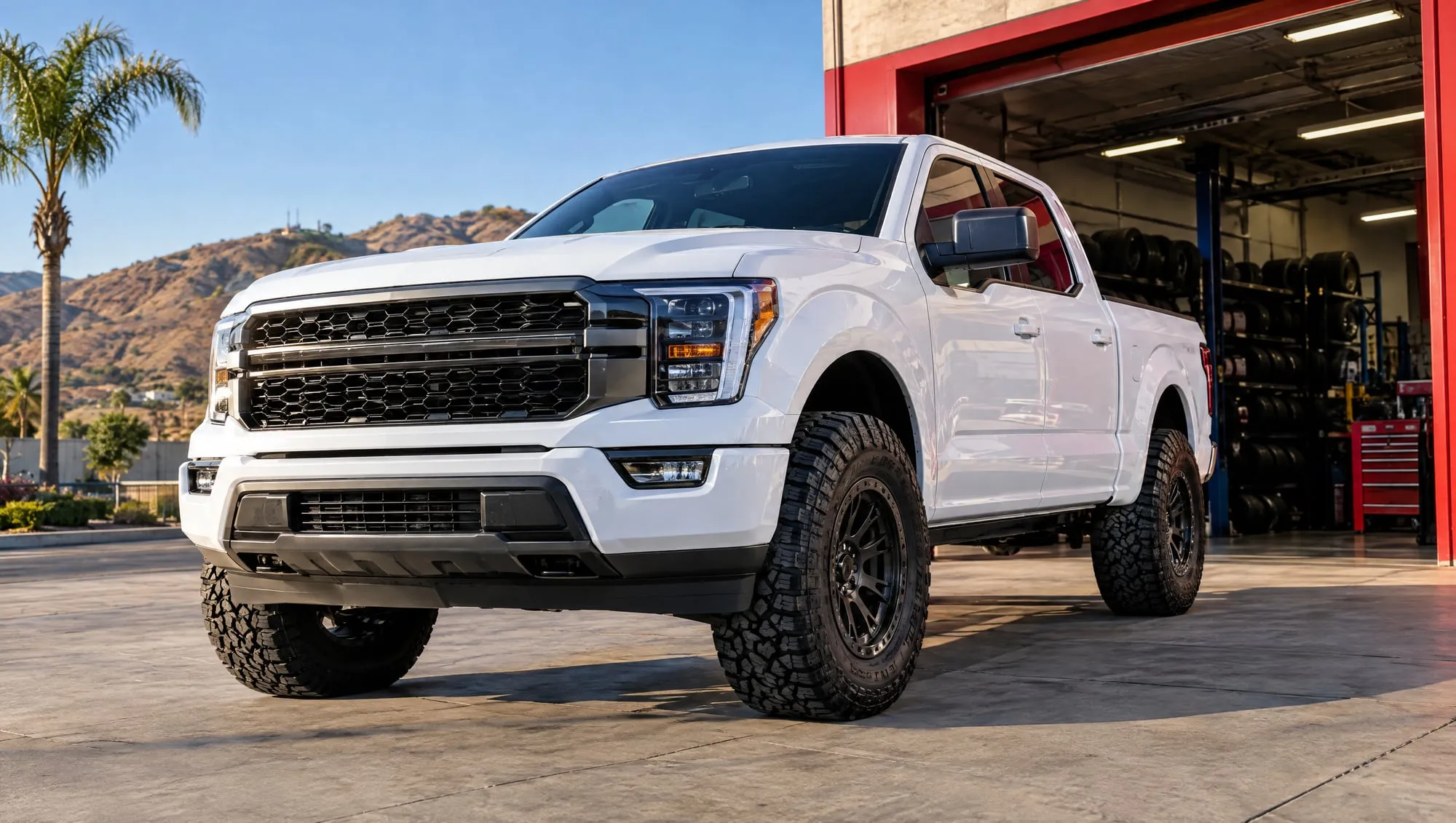 White pickup truck on new all-terrain tires parked outside a tire shop bay