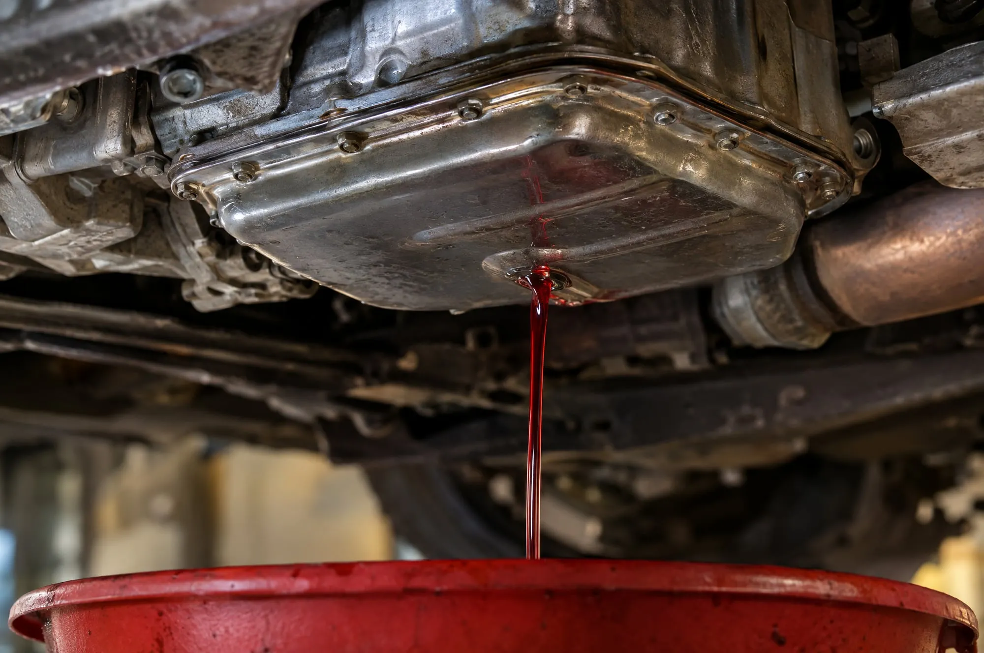 Red transmission fluid draining from a transmission pan into a red drain pan