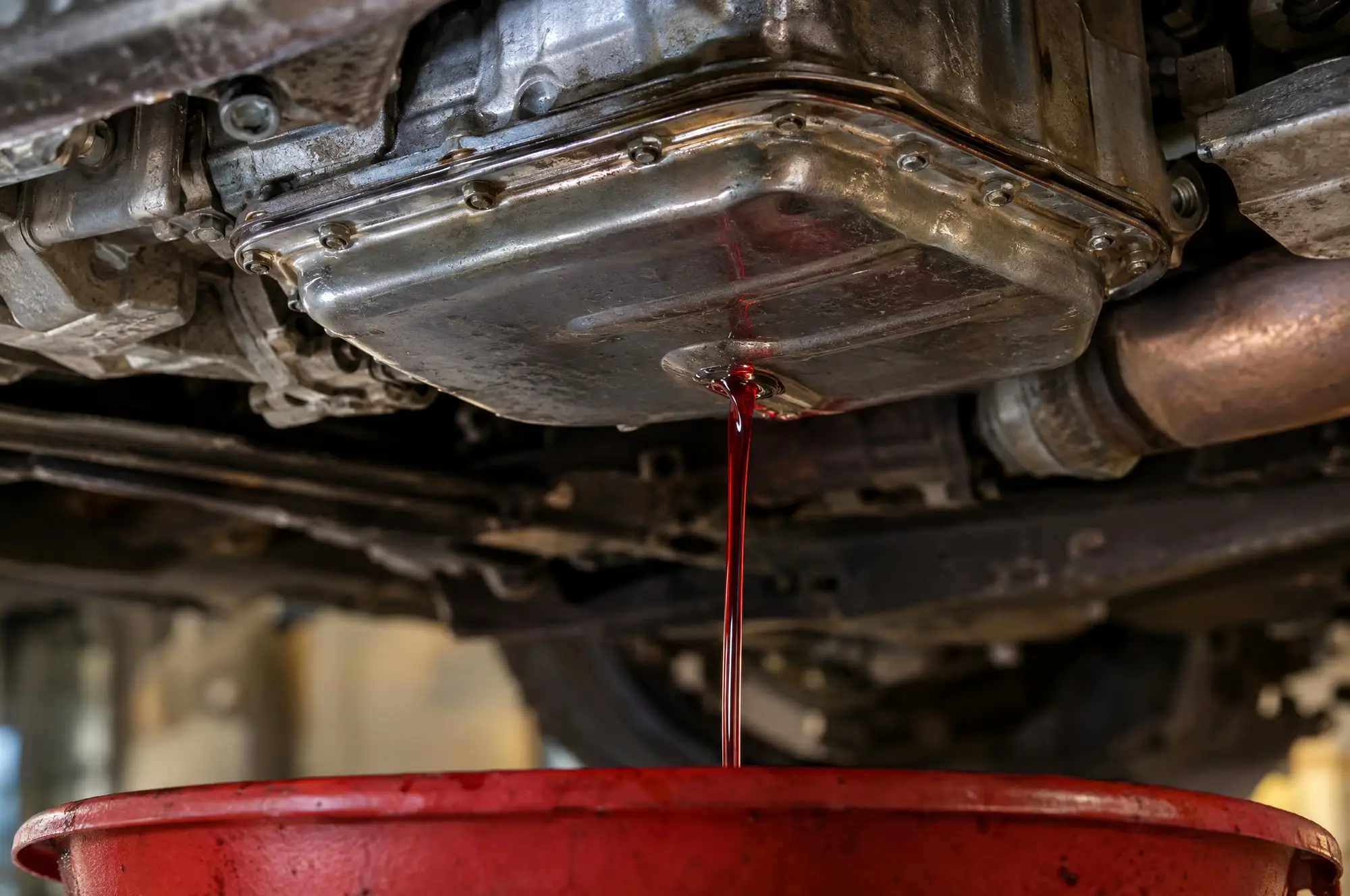 Red transmission fluid draining from a transmission pan into a red drain pan