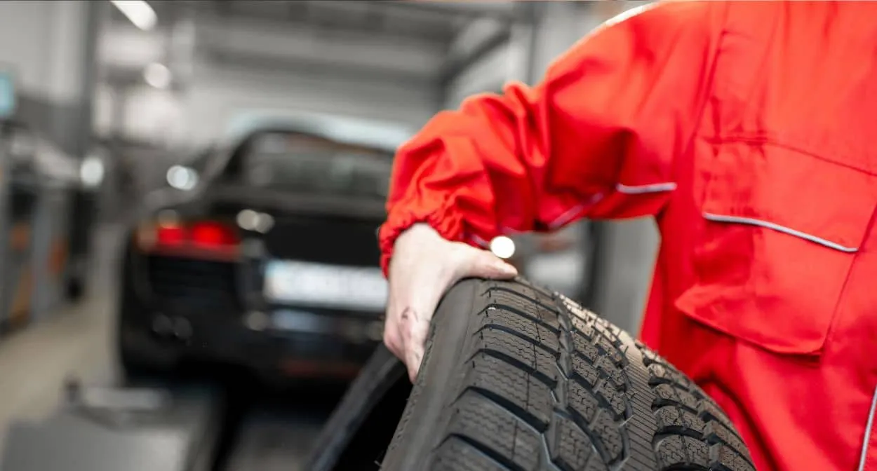 Technician in a red uniform rolling a new tire through the service bay