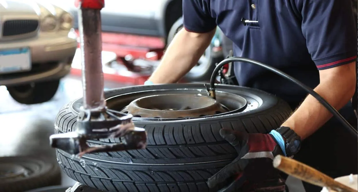 Technician in gloves fitting a new tire onto a wheel with a tire changer